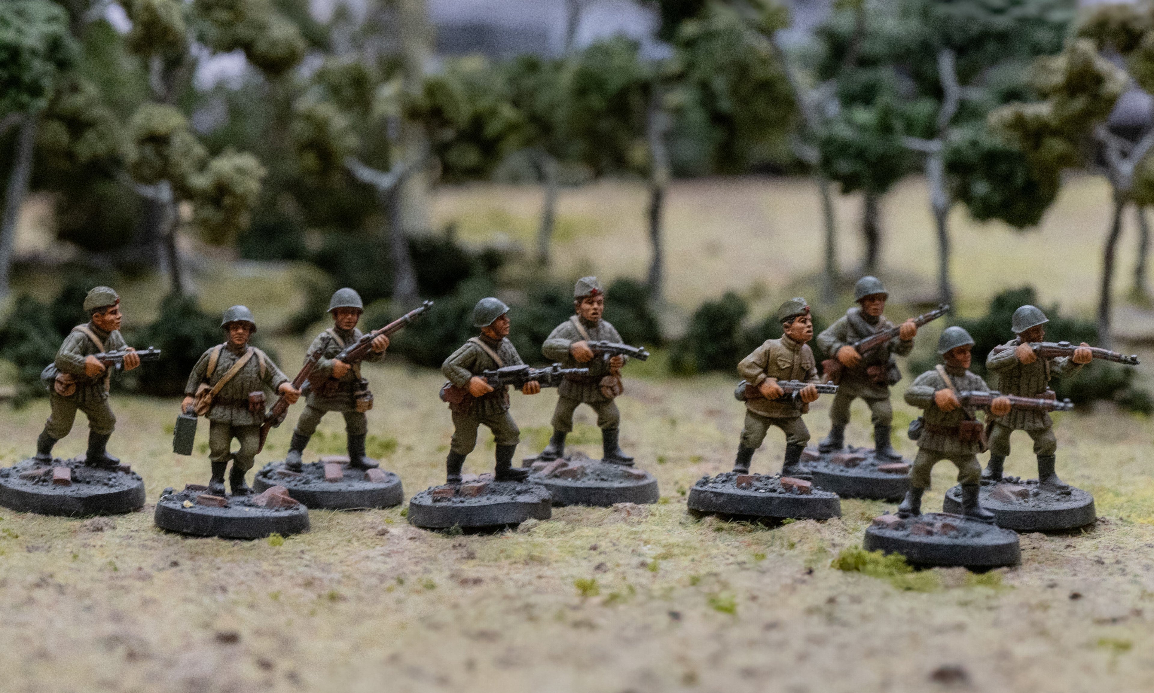 Miniature model soldiers on a grassy field with trees in the background